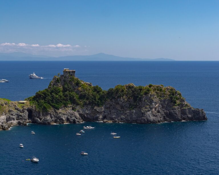 a rocky island with boats with Isola Bella in the background